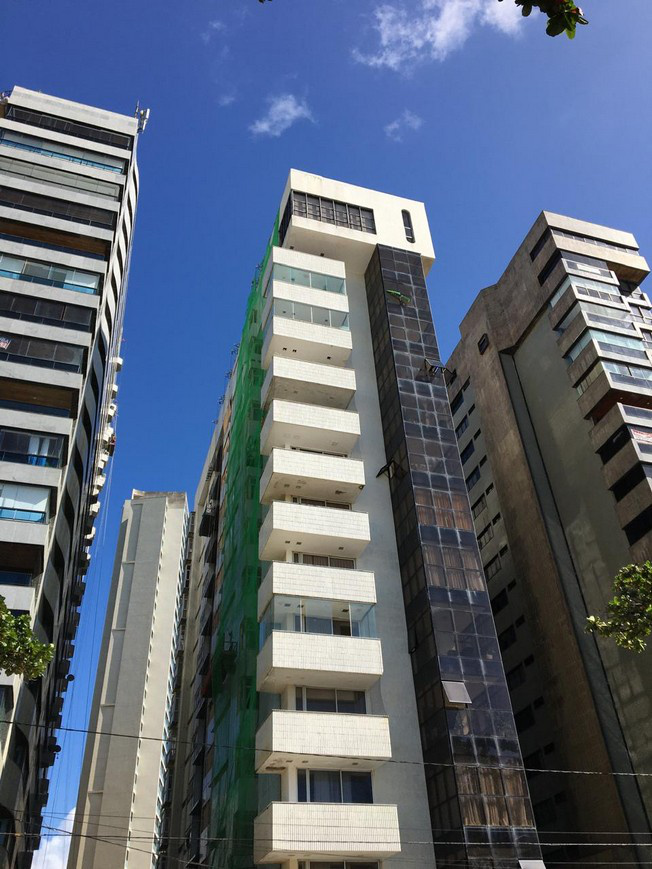 Multi-storey residential tower seen from grade with protective netting installed over one elevation while the adjacent elevations remain exposed