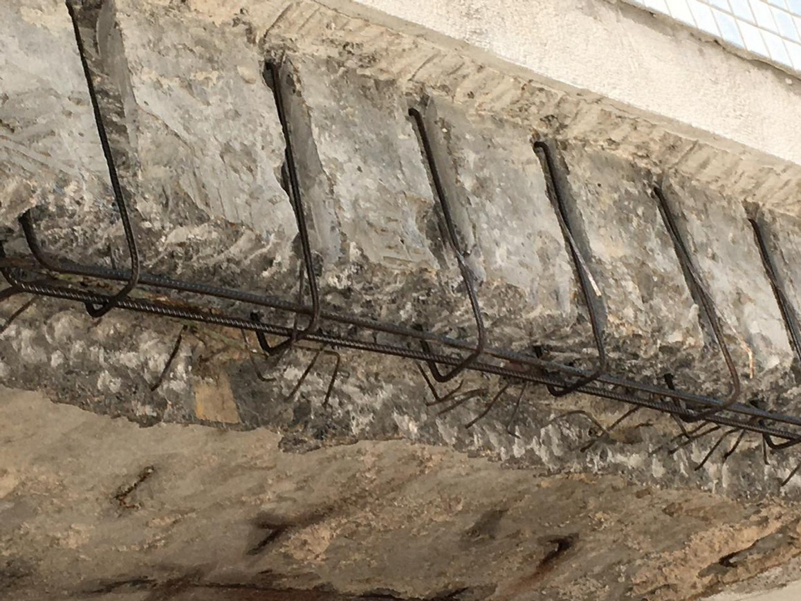 Concrete removed from the underside of a beam, exposing stirrups and longitudinal reinforcing bars along the opened repair area
