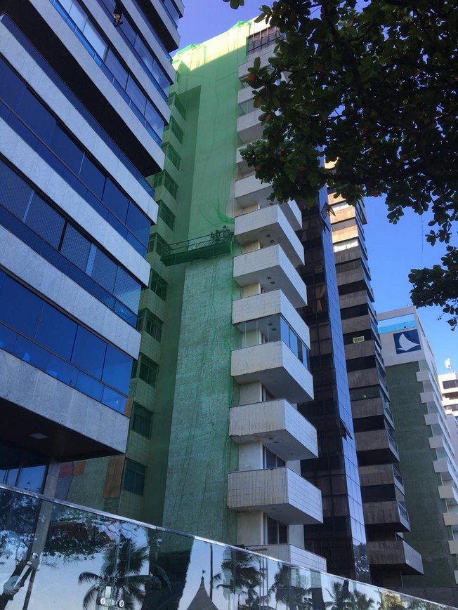 Residential façade covered by green protective netting with a suspended work platform positioned beside the elevation