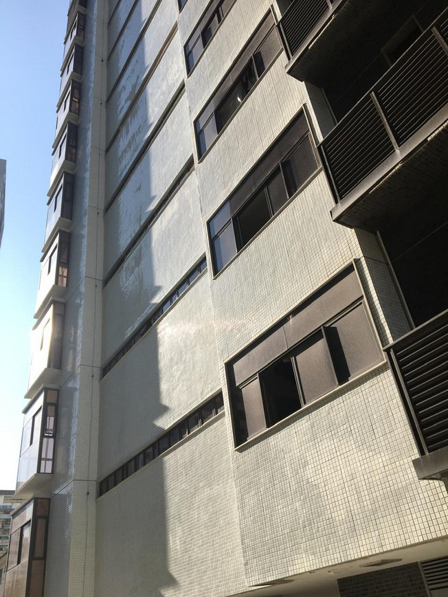Multi-storey residential façade with balcony stacks, window bands and a restored tiled wall surface seen from grade