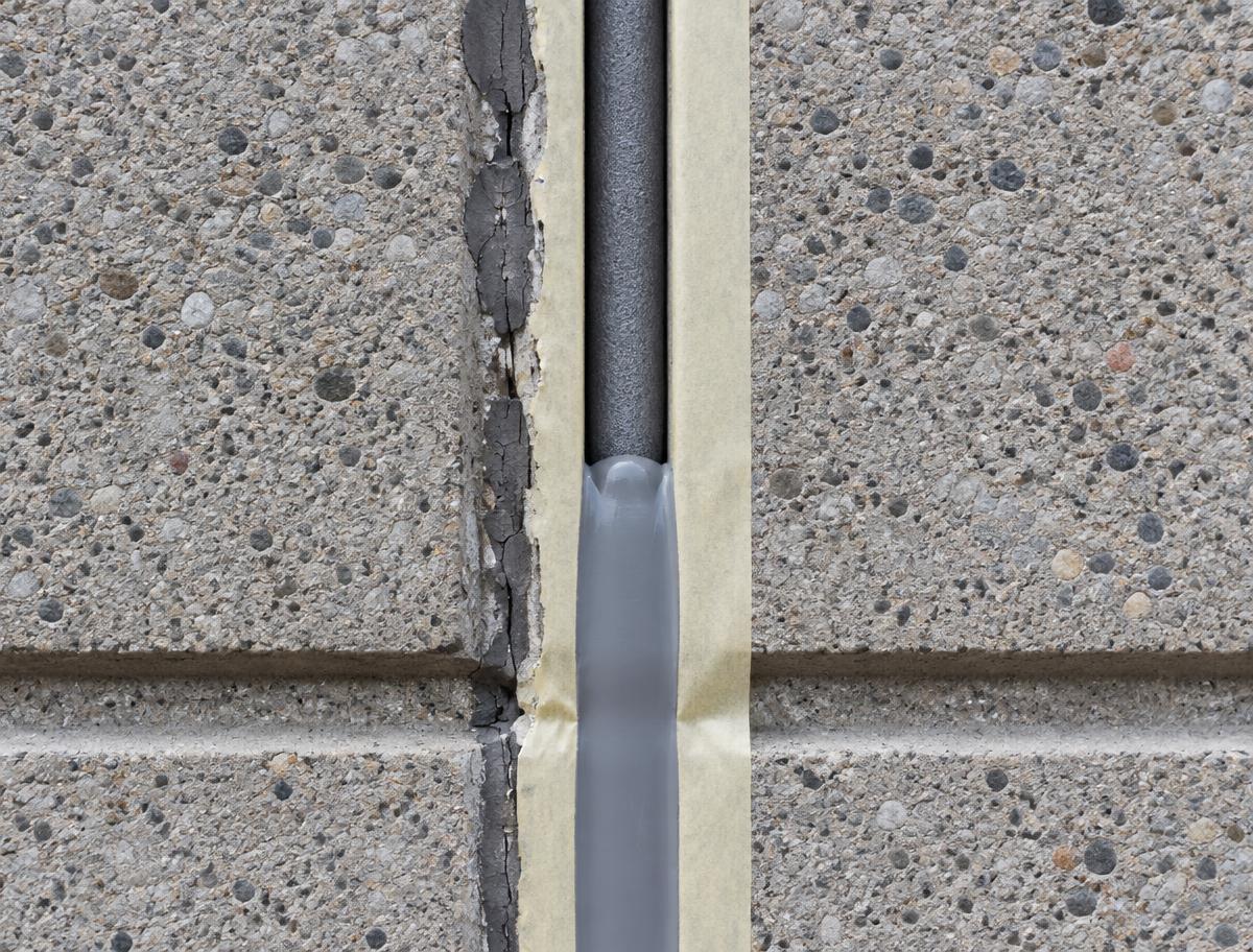 Illustrative vertical expansion joint with old cracked sealant removed, backer rod installed and new grey sealant tooled between masked edges